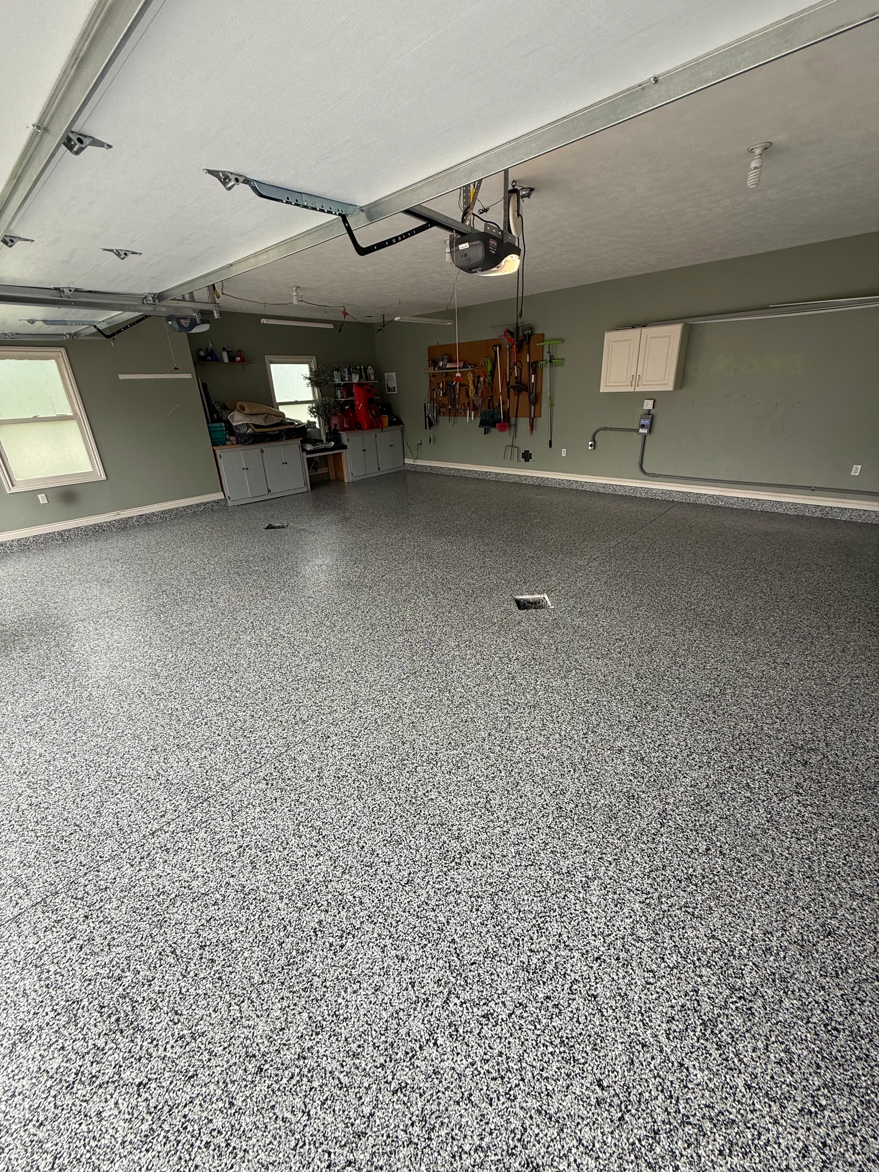 Spacious garage with gray speckled epoxy floor, sage walls, and white cabinetry