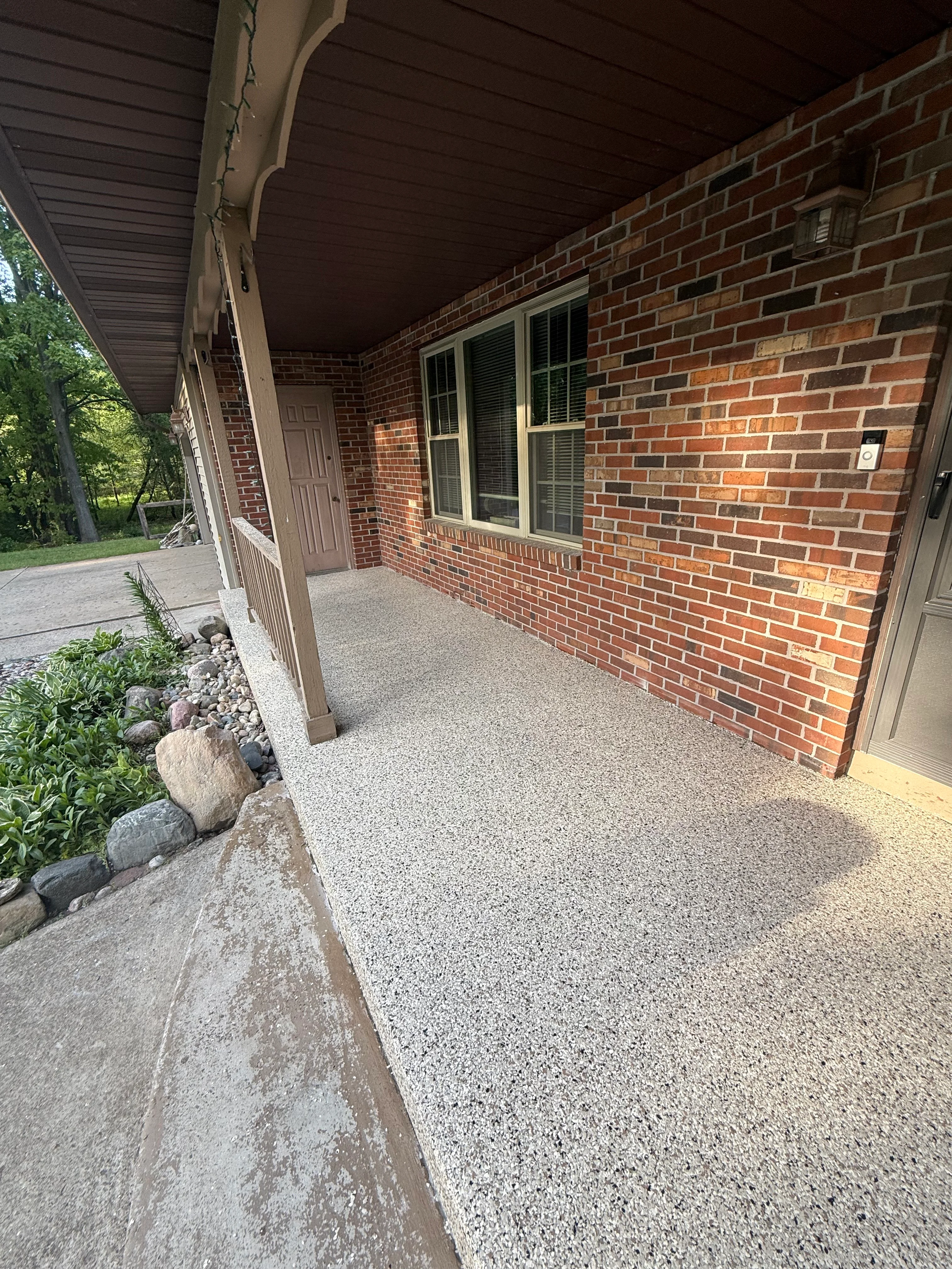 Newly coated concrete porch with gray aggregate finish in front of brick home