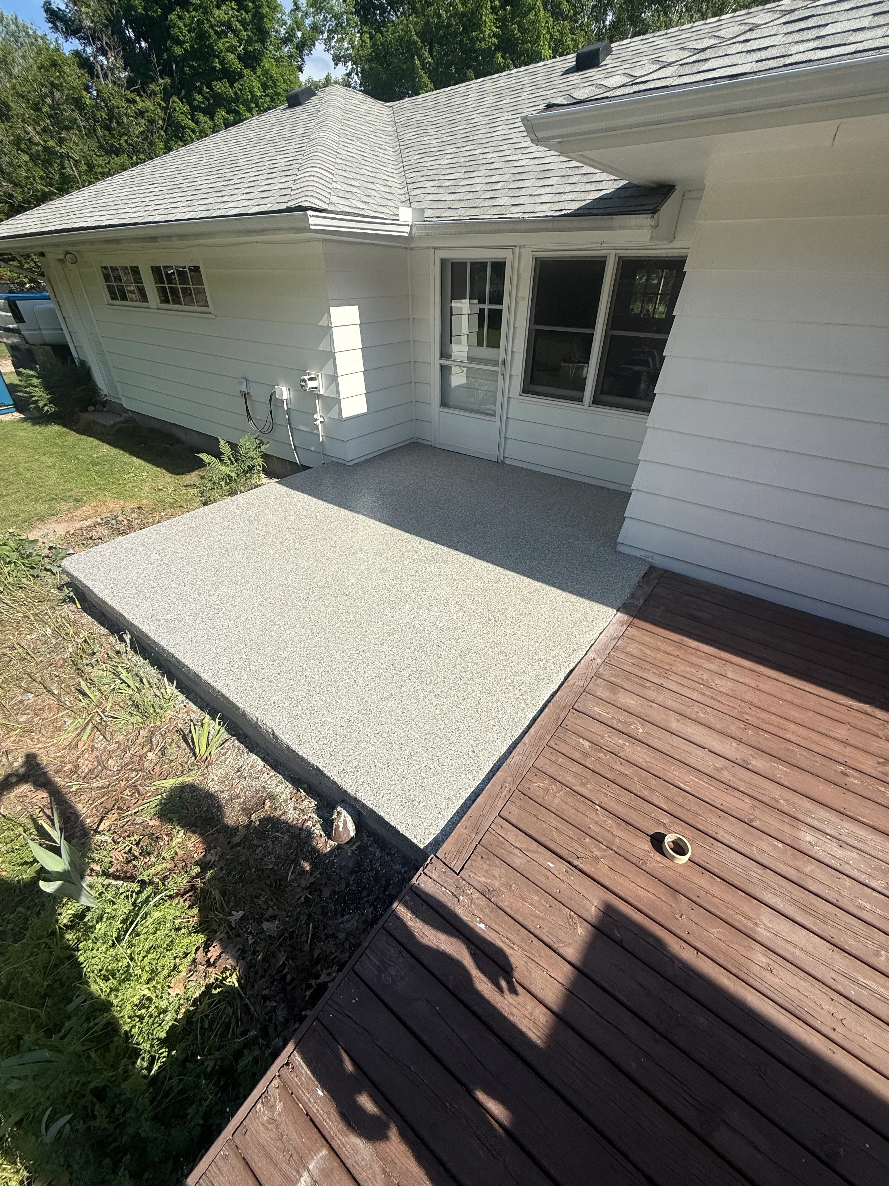 Light gray concrete patio with aggregate finish next to brown composite deck and white house