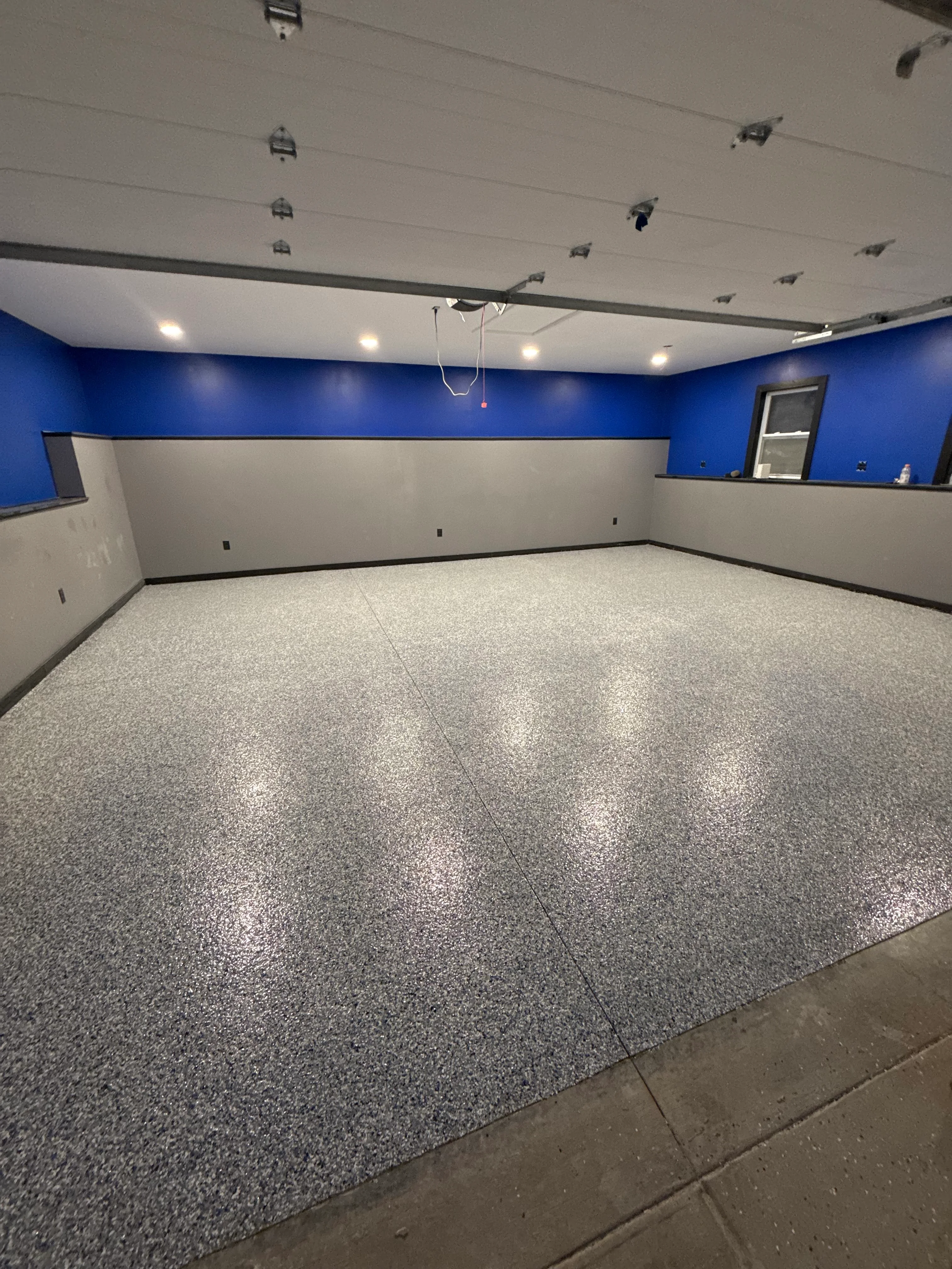 Finished epoxy garage floor with gray speckled coating and blue accent walls